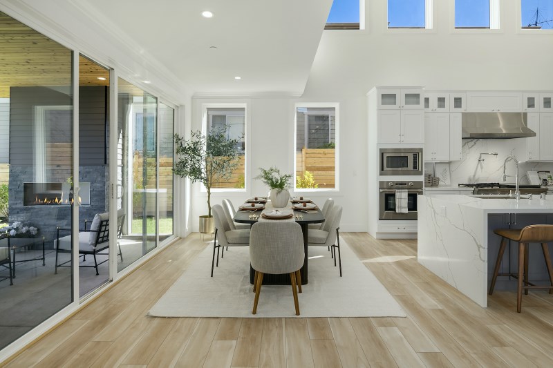 Bright open-concept dining area and white kitchen featuring light sandy brown luxury vinyl plank flooring.