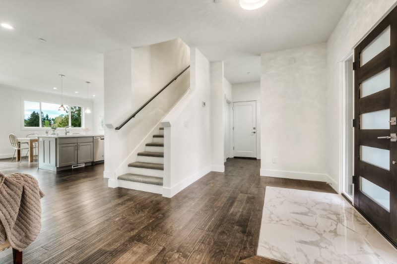 Entry hall with a staircase and wood-look plank flooring leading toward an open kitchen.